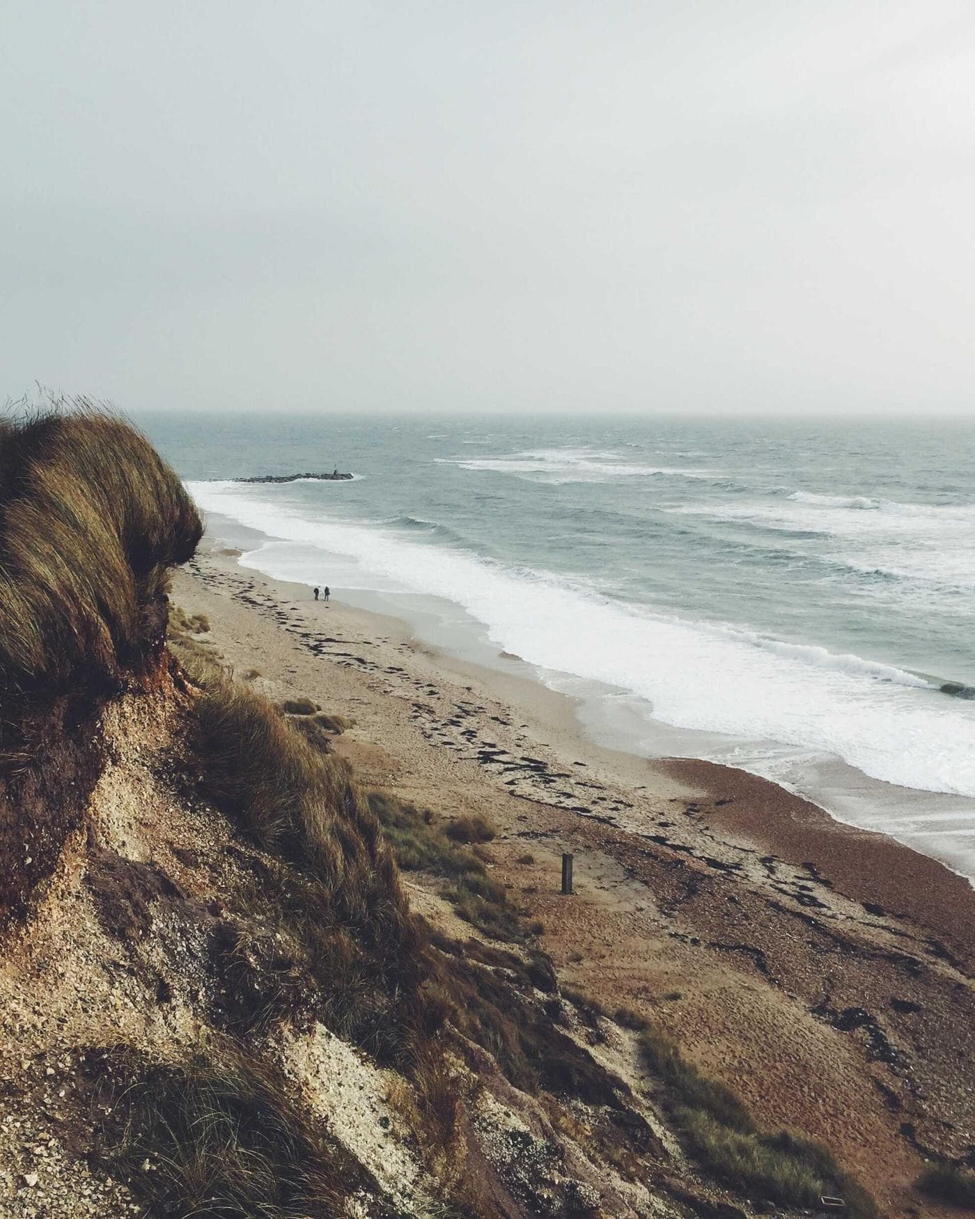 Zwei kleine Gestalten am weiten Strand, graue See